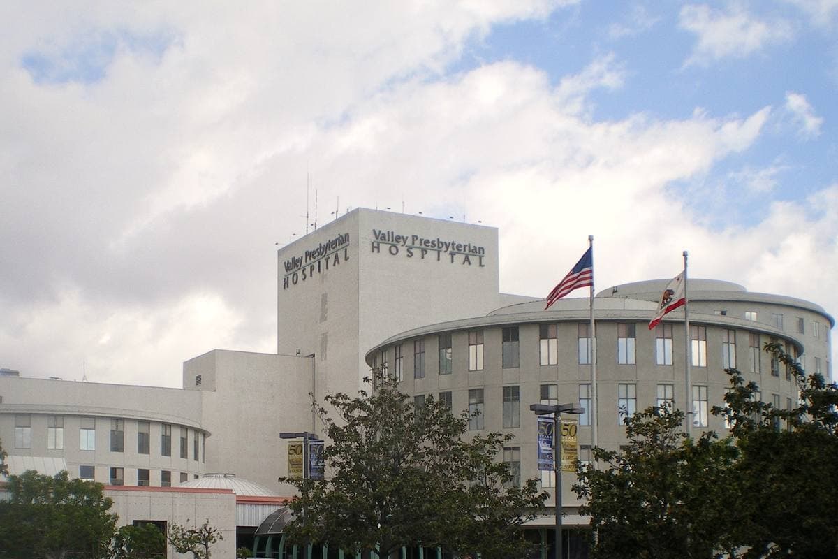A white hospital block with a rounded wing and flags in front, under a cloudy sky