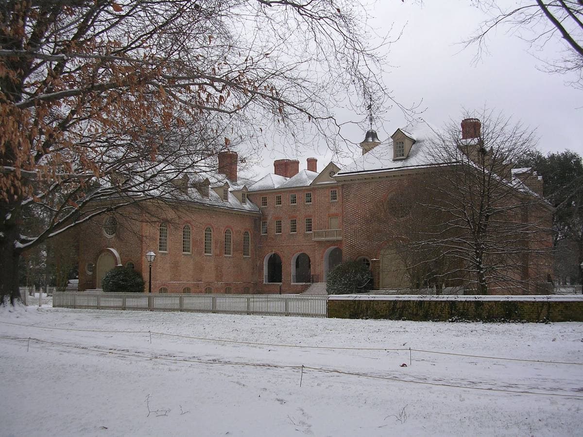 A long red-brick colonial college building with a cupola, seen across a snowy lawn