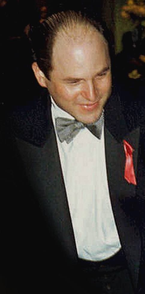 Jason Alexander in a tuxedo with a red ribbon on his lapel