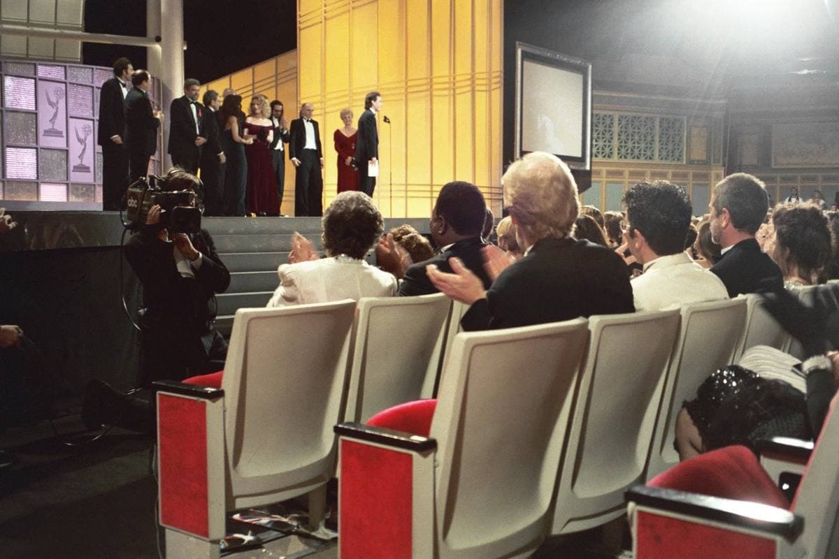 Colour photograph from the audience at the 1993 Emmy Awards: empty cream theatre seats in the foreground, the cast collecting the award on a gold stage