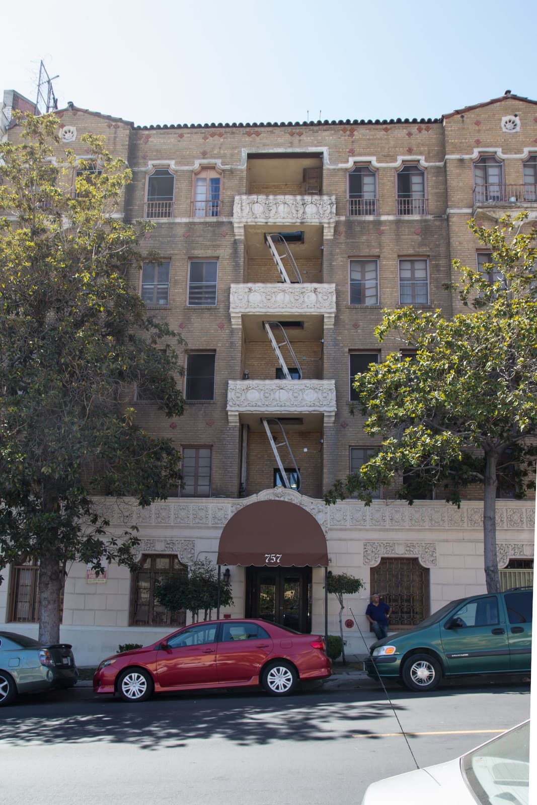 A five-storey brick apartment building with a fire escape and an awning over the door
