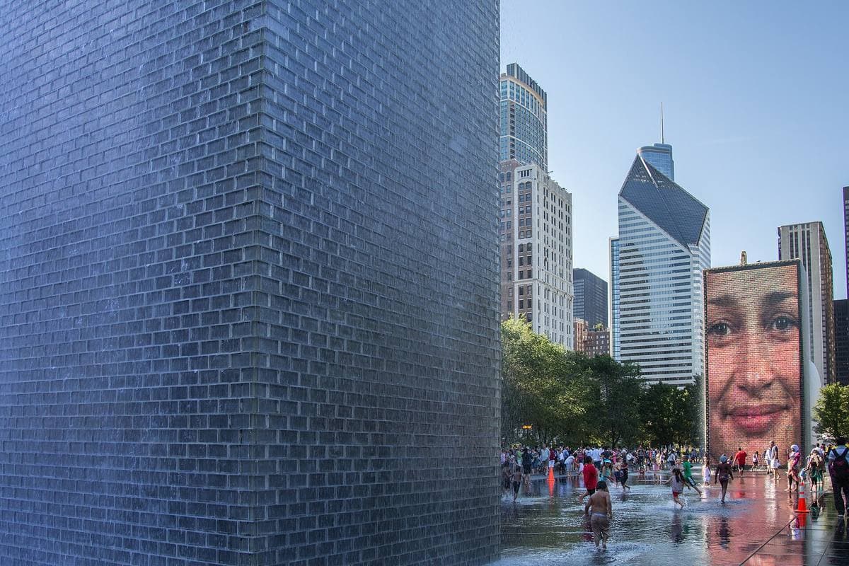 A glass-brick tower showing a giant face over a shallow pool where children play