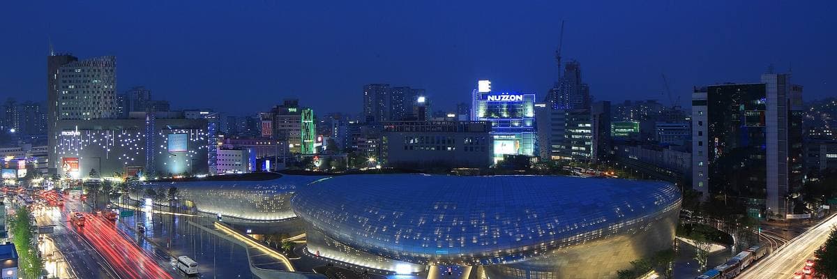 A long curving silver building lit at night among city towers