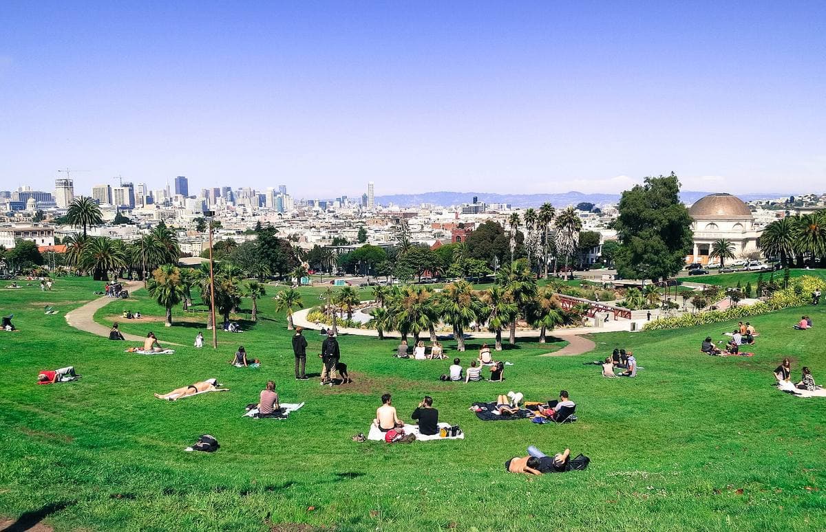 People sitting on a sloping green lawn with the San Francisco skyline in the distance