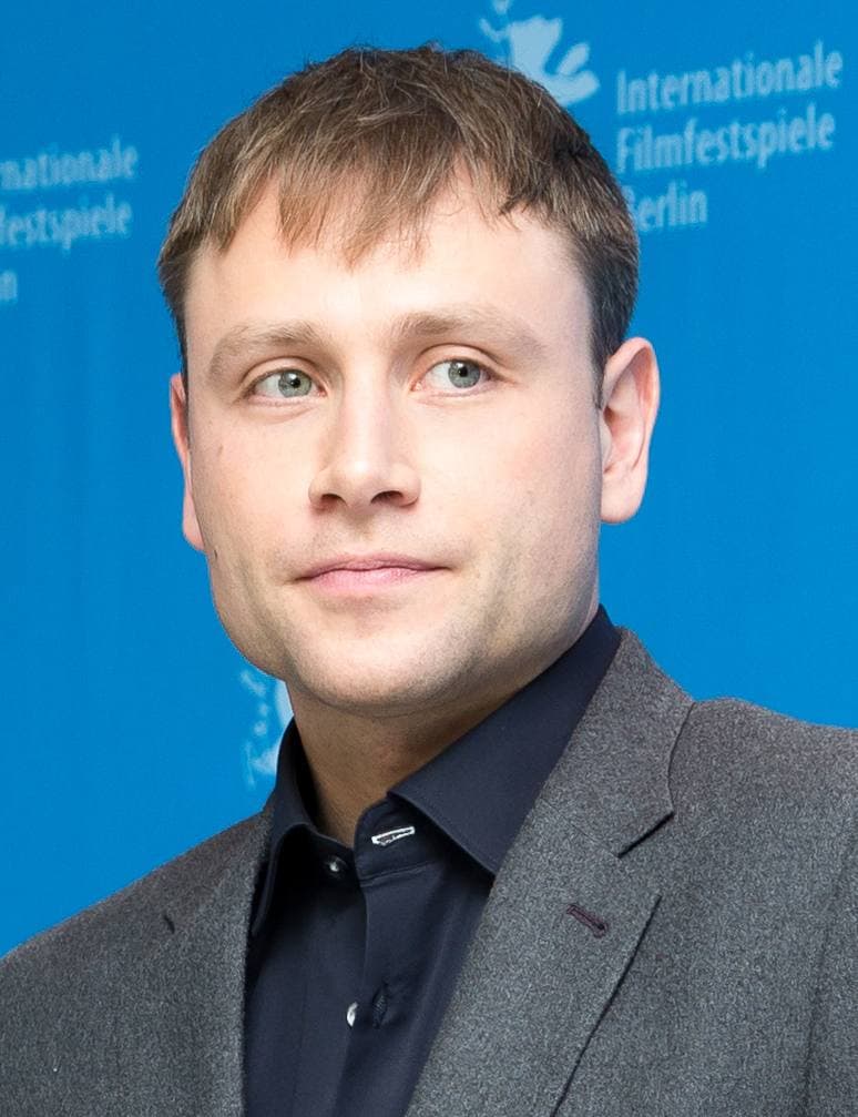 Max Riemelt in a grey jacket against a blue festival backdrop