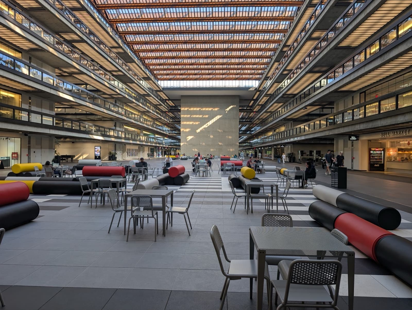 A vast glass-roofed atrium with tables, sofas and tiers of offices either side