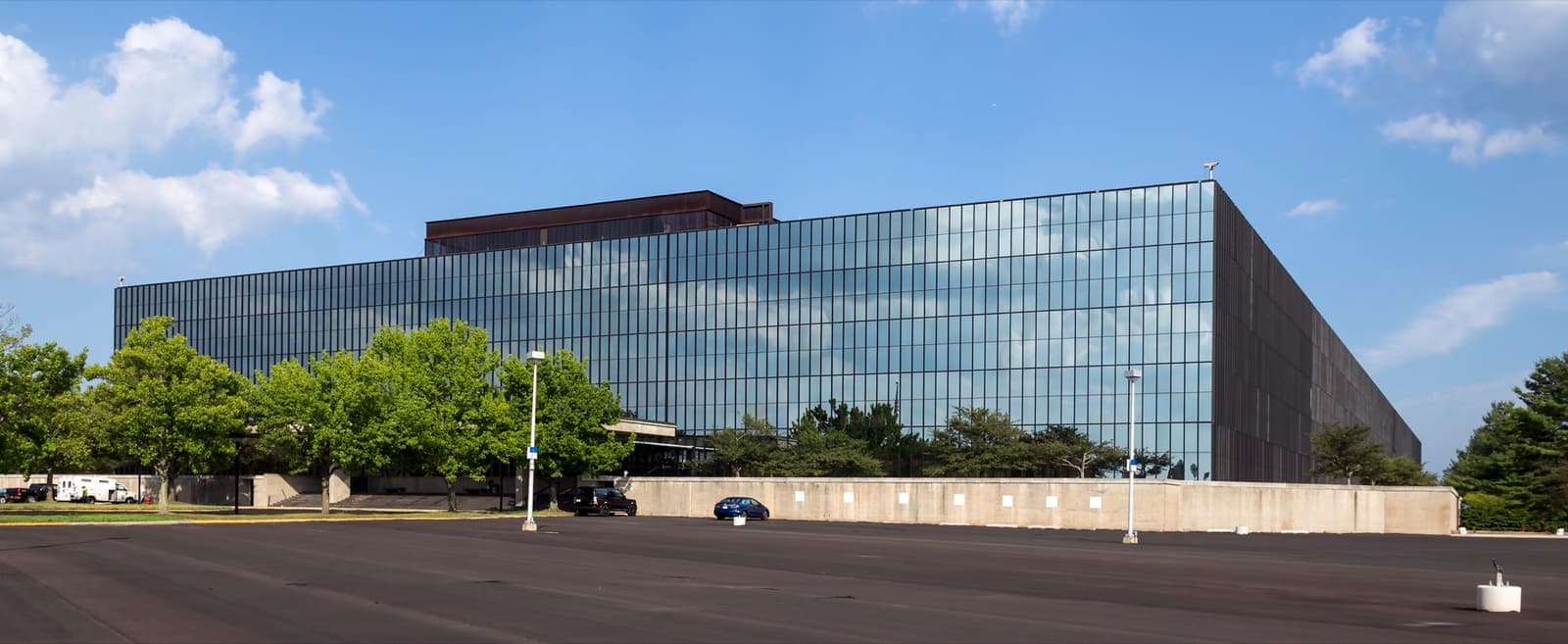 A long, low building clad entirely in dark mirrored glass beyond a car park