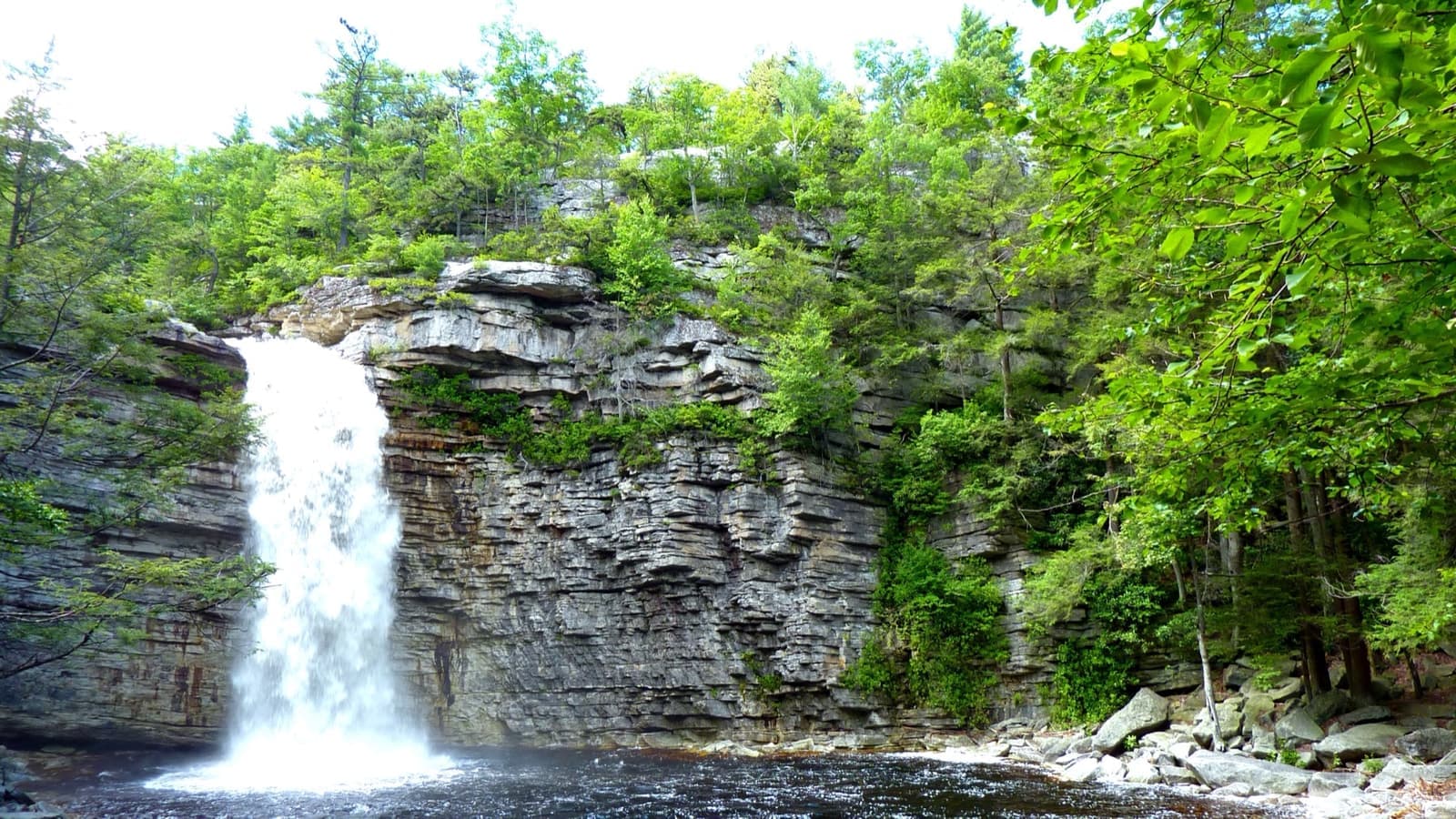 A waterfall pouring over a layered rock ledge into a pool