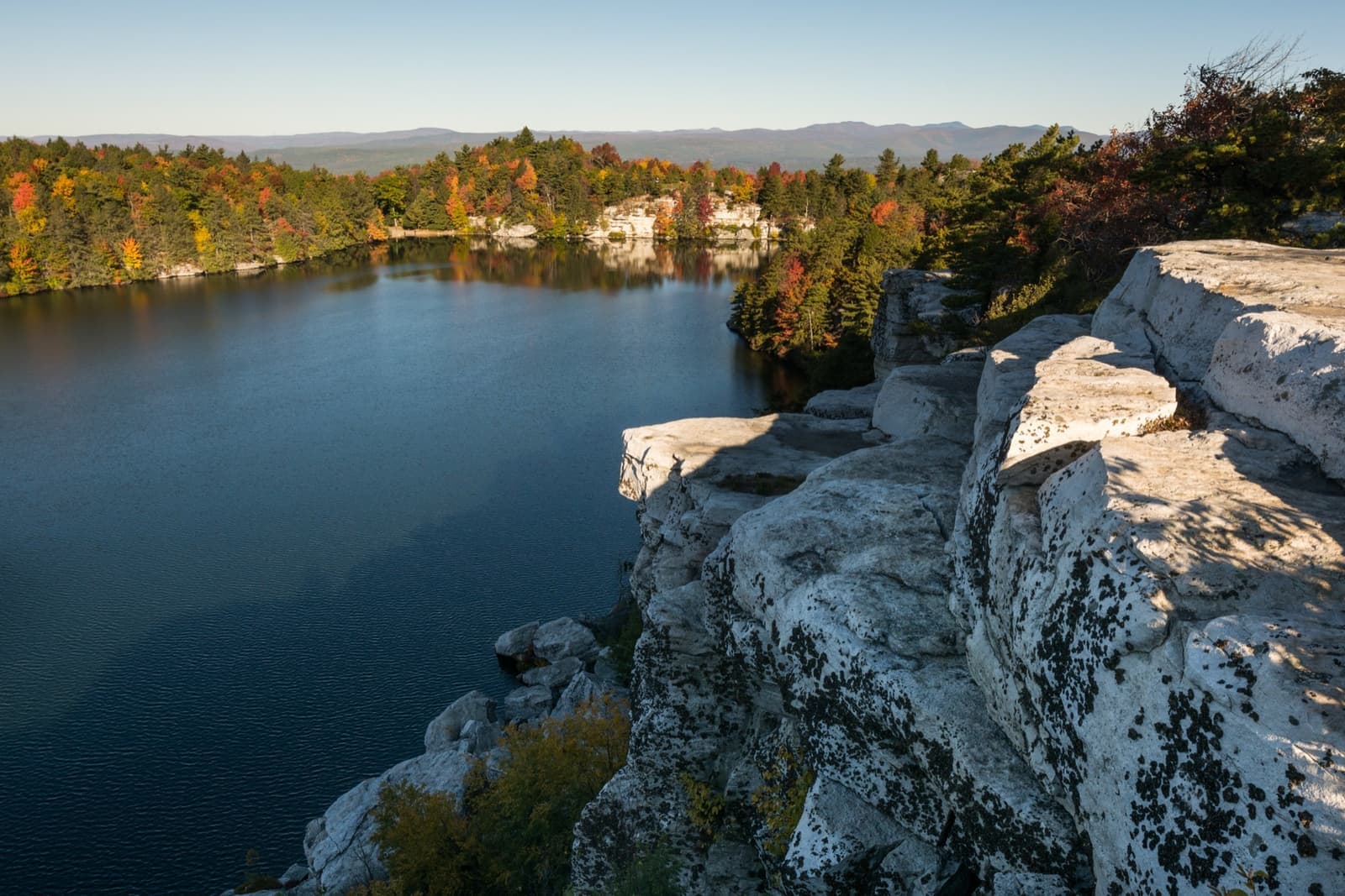 A dark lake below white cliffs, autumn trees and distant hills