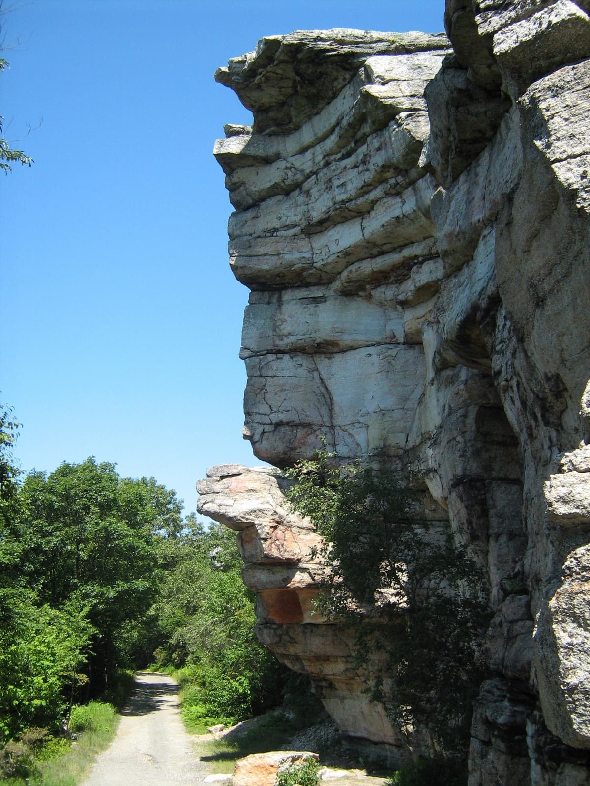 A tall pale rock cliff beside a path under blue sky