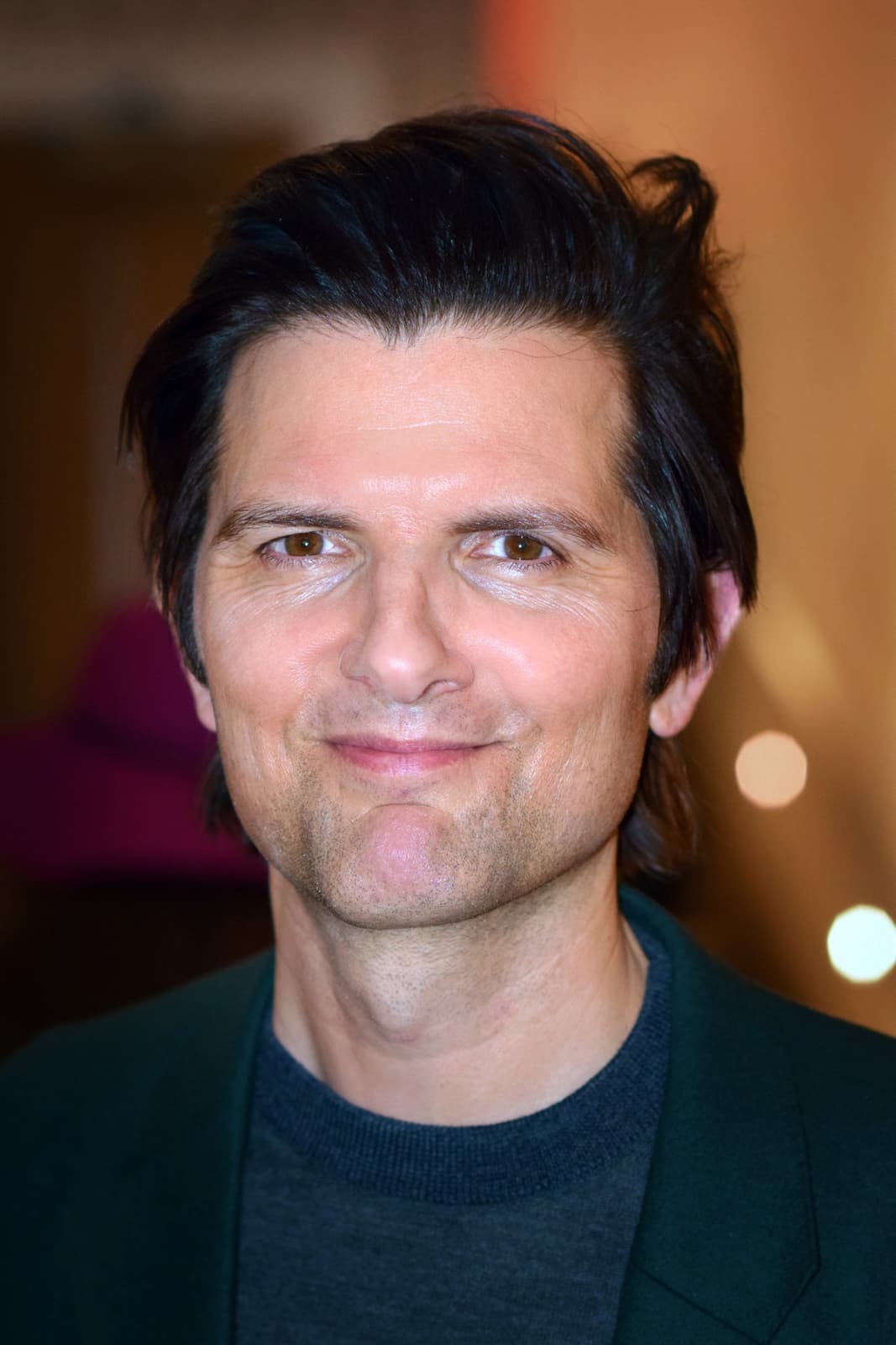Adam Scott smiling at the camera, dark hair swept back