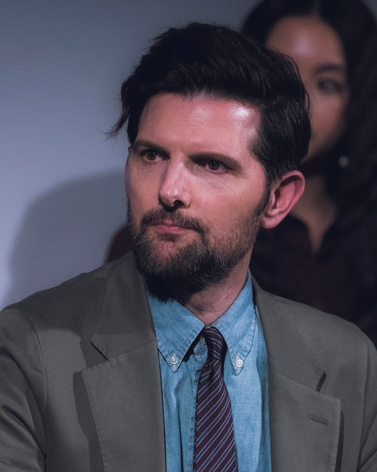 Adam Scott, bearded, in a grey suit and tie