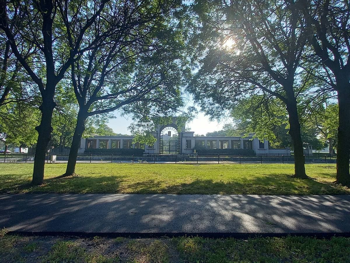 A stone garden gate under tall trees with sunlight through the leaves
