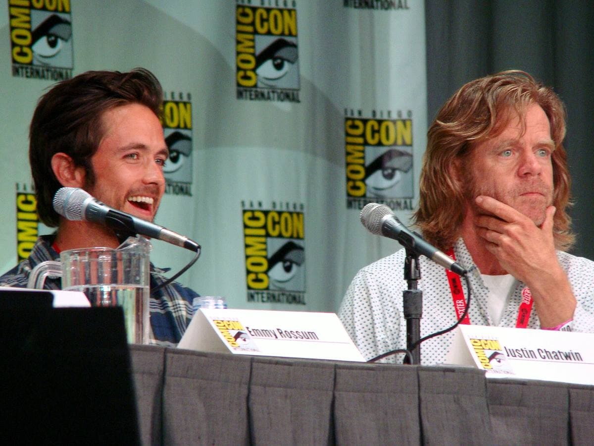 William H. Macy laughing at a panel table, chin on his hand