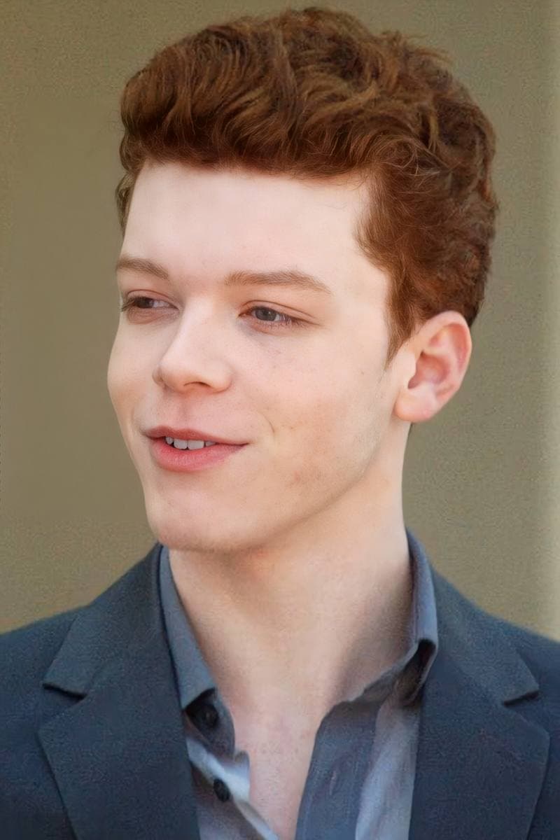 Cameron Monaghan, red hair, in a grey jacket, looking to one side