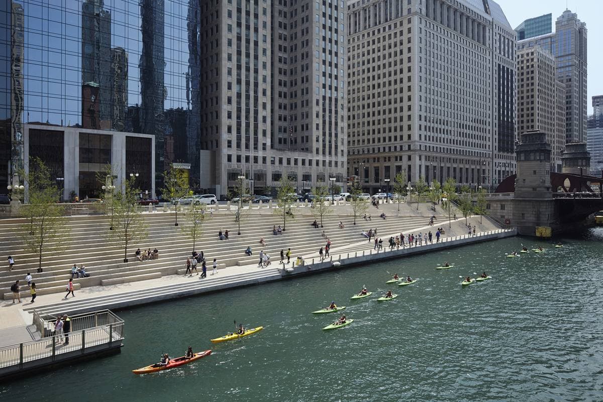 Kayakers on the Chicago River beside a stepped riverside walk and towers
