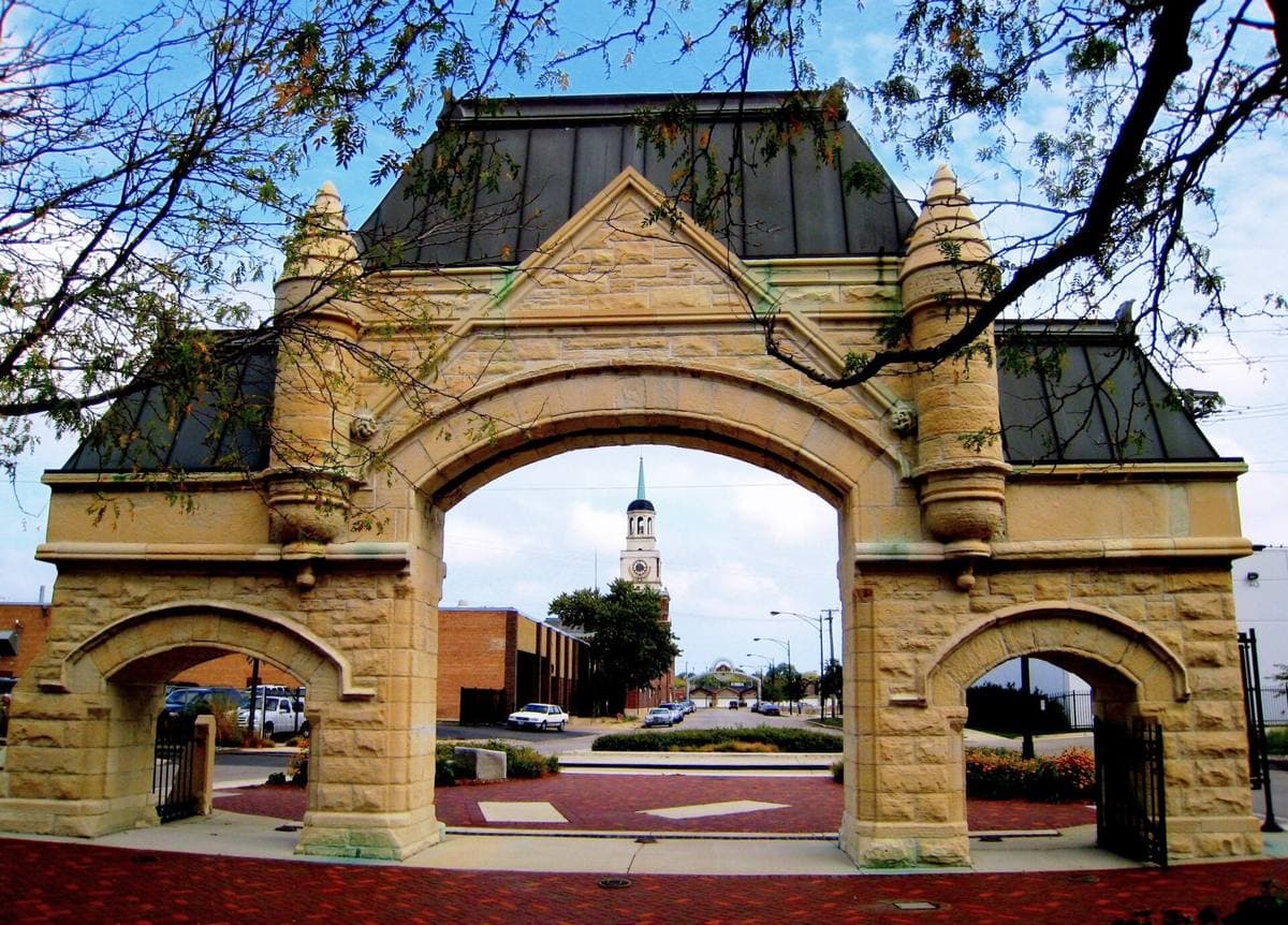 A limestone triple-arched gate with a steeply pitched copper roof