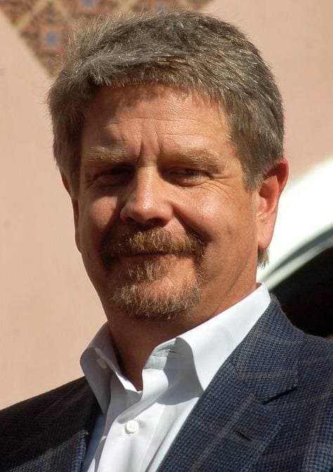 John Wells, grey hair and beard, in an open-necked shirt