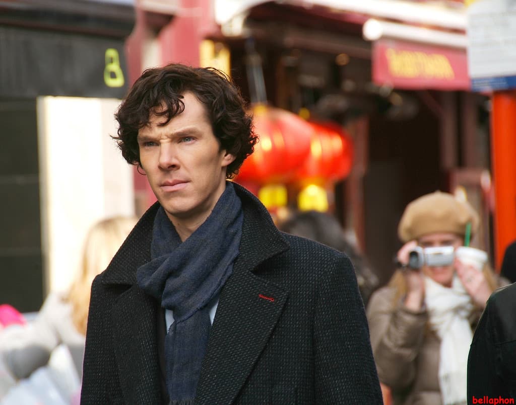 Benedict Cumberbatch in a dark coat and blue scarf on a Chinatown street, red lanterns behind