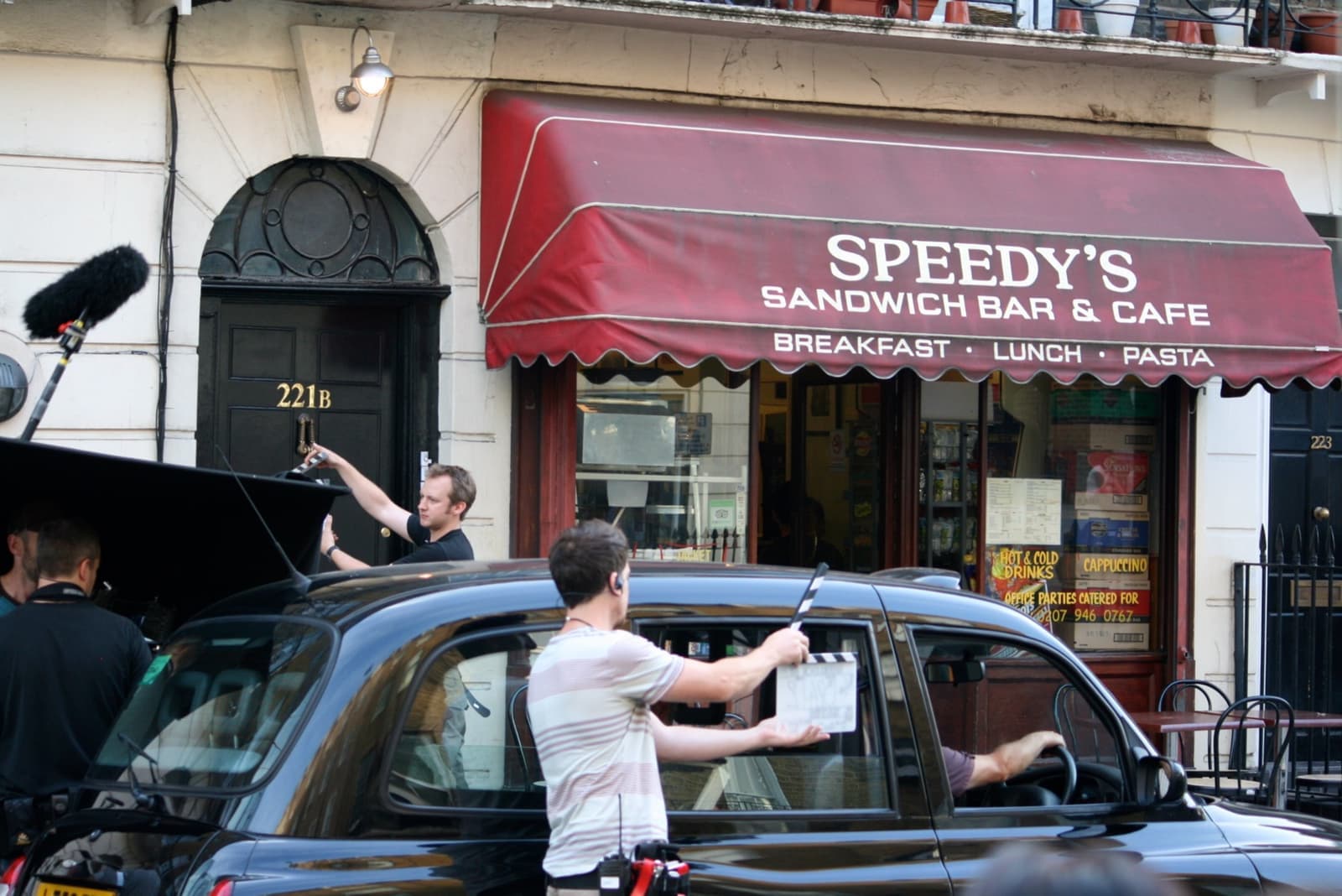 A film crew and a black taxi outside Speedy’s café and the black door marked 221B