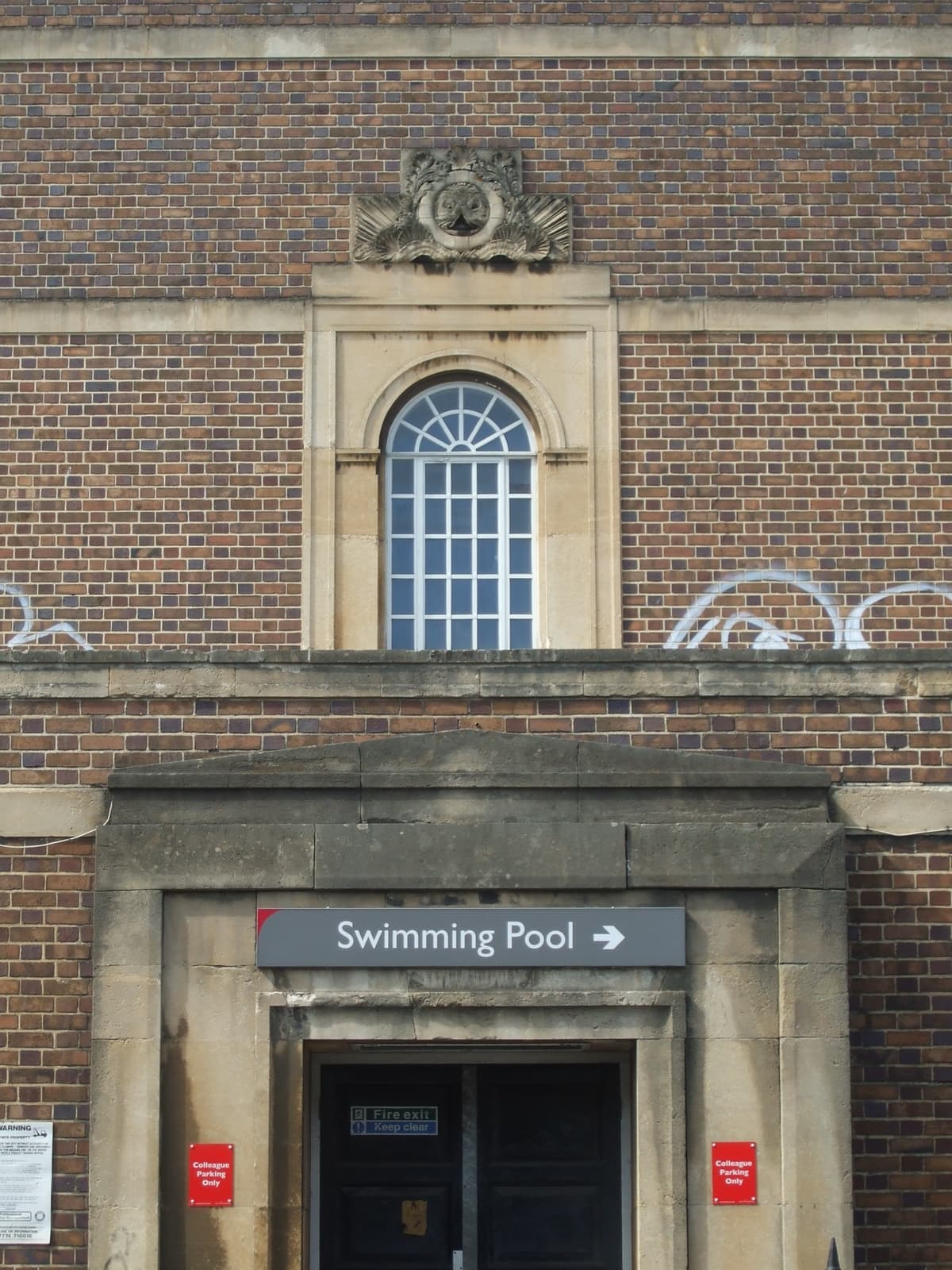 A brick 1930s entrance with an arched window and a sign reading Swimming Pool
