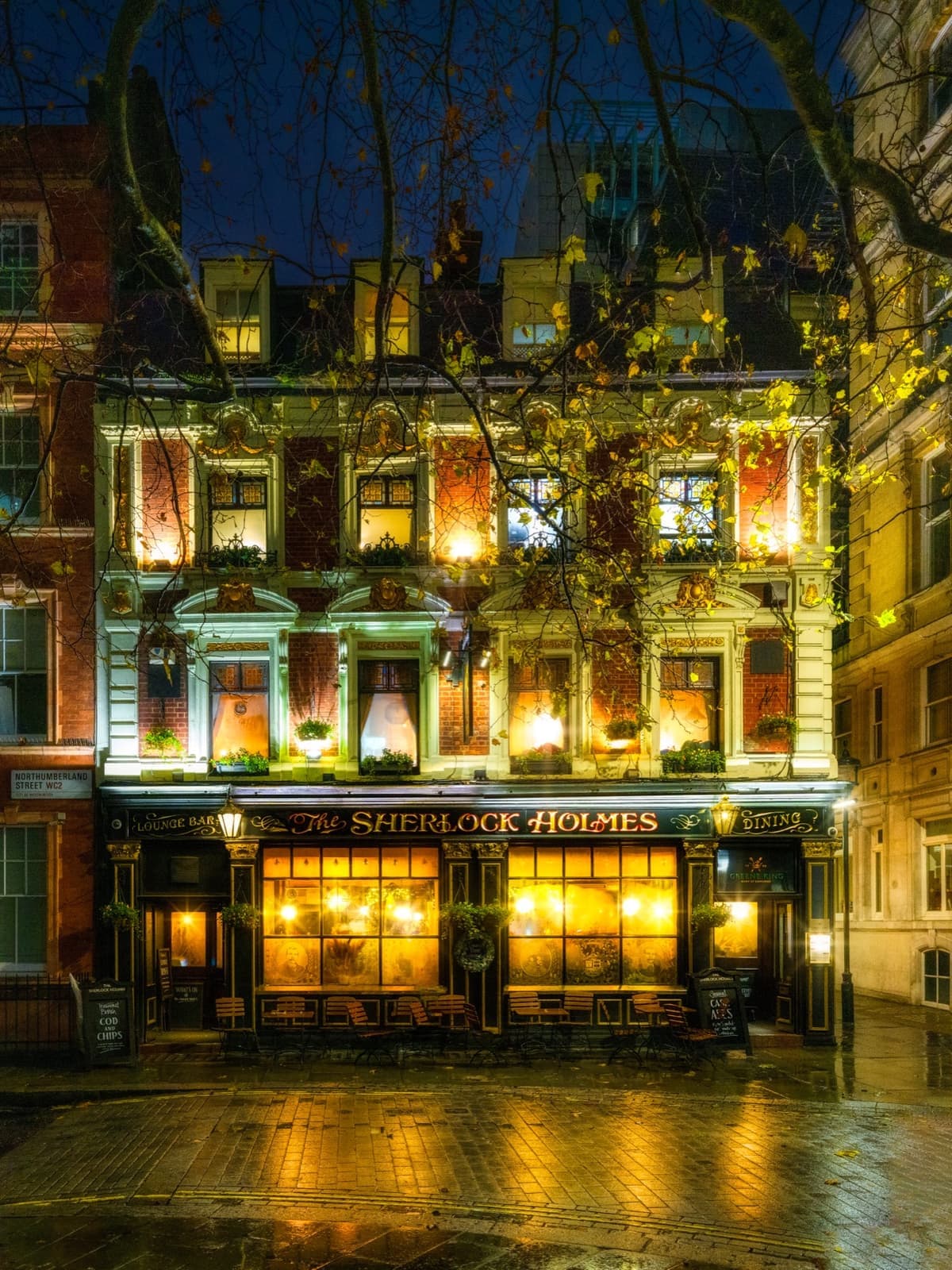 A Victorian pub front lit gold at night on a wet street