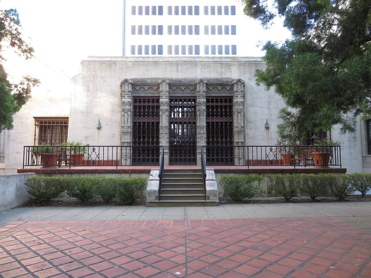 A pale classical building with arched windows behind palms