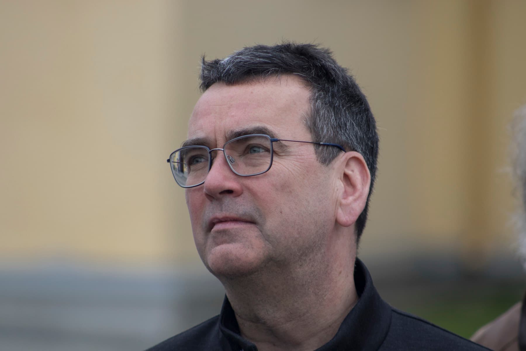 Mick Herron in glasses and a dark jacket, looking up and to the side