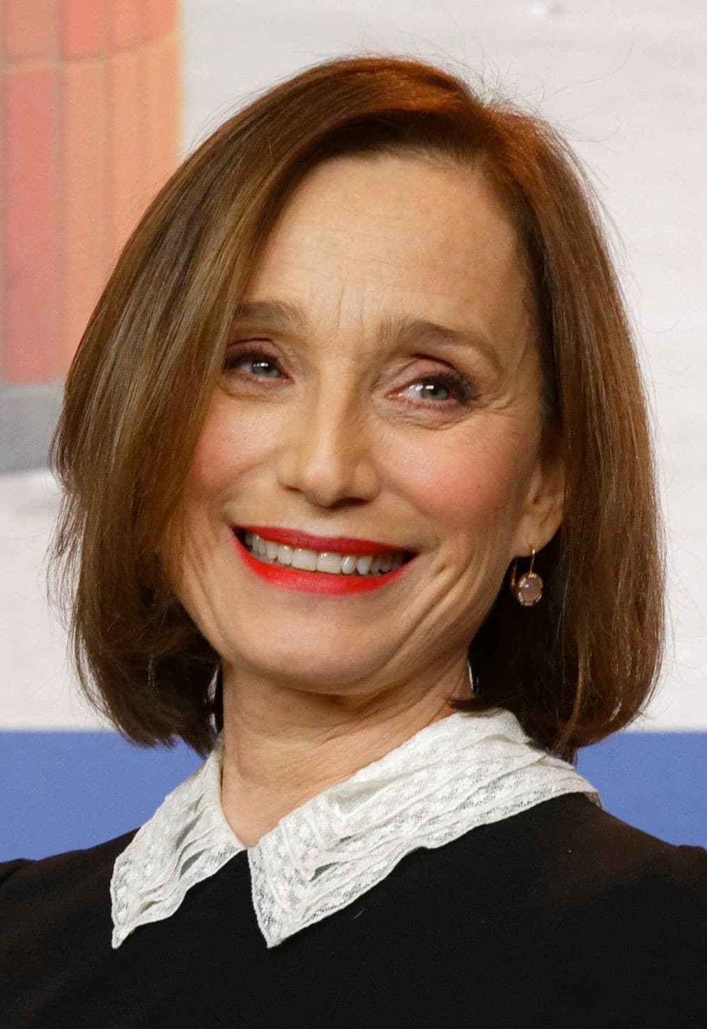 Kristin Scott Thomas smiling, in a black dress with a white lace collar