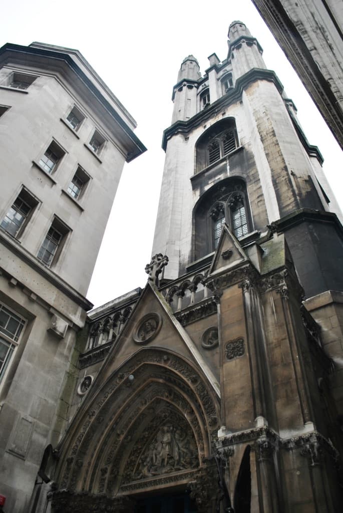 The Gothic stone tower and carved porch of St Michael, Cornhill, between office buildings