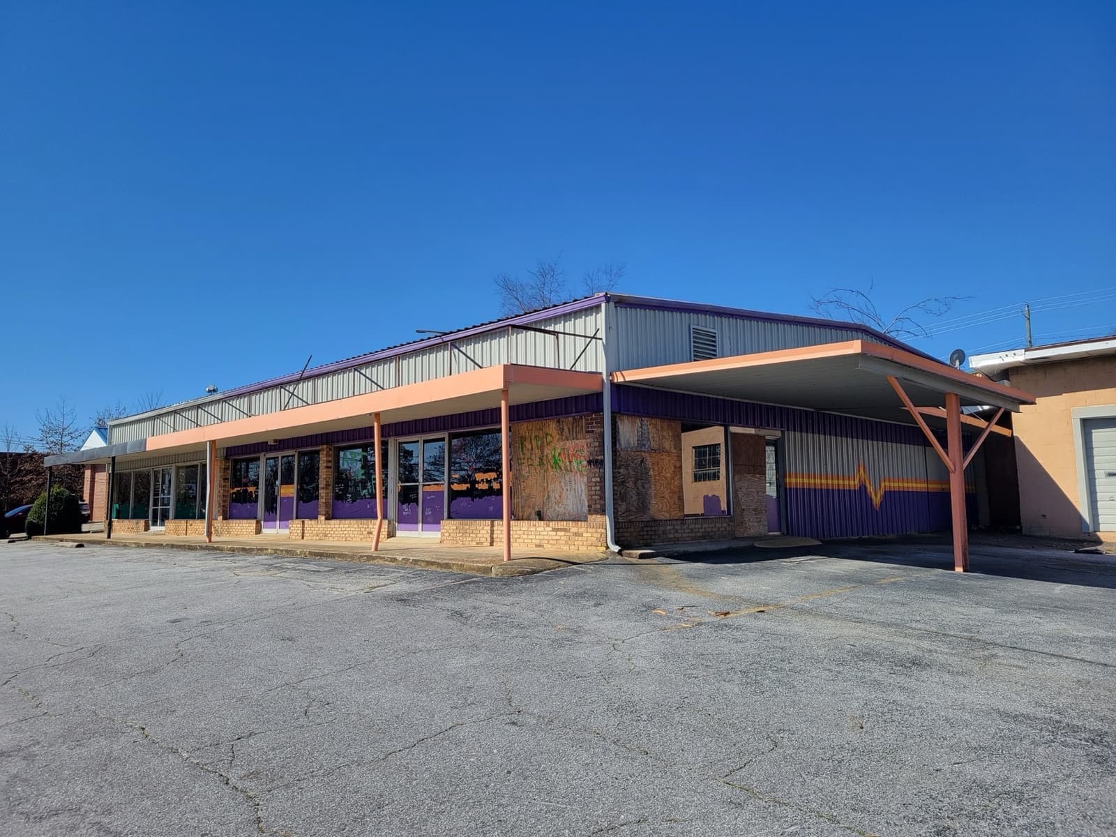 A low purple and orange shopfront row behind an empty car park under blue sky