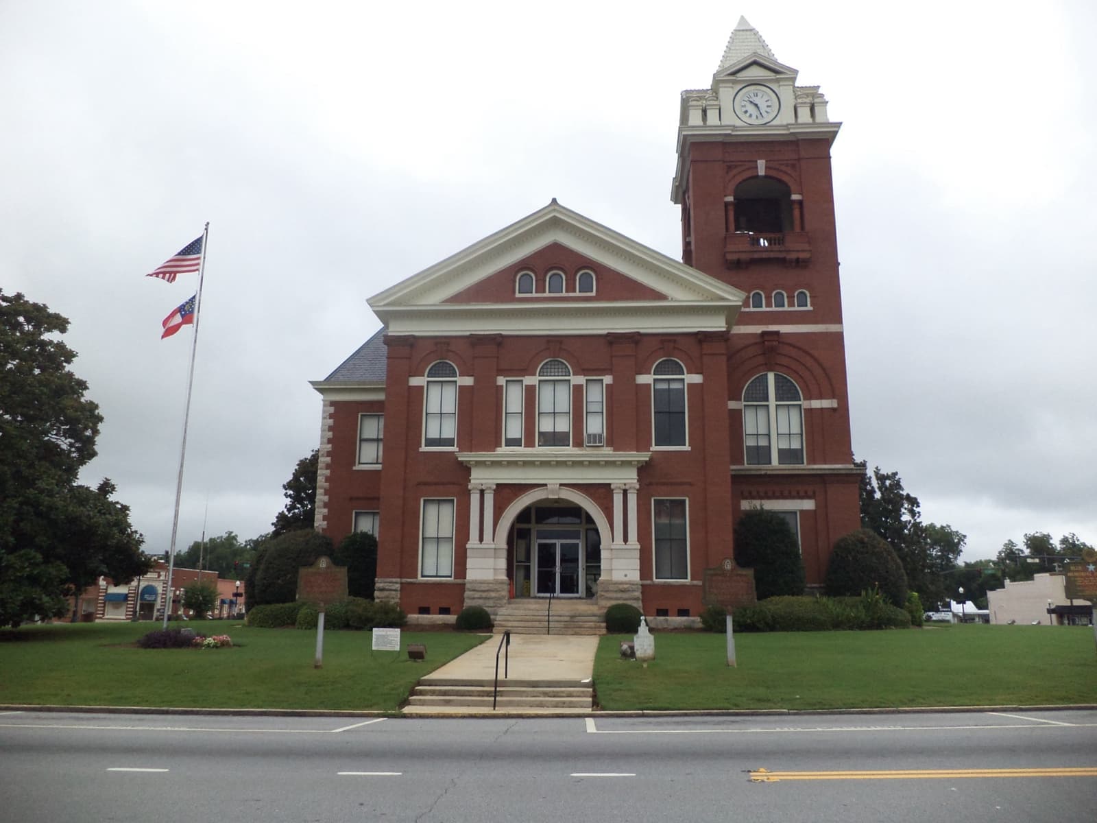 A red-brick courthouse with a clock tower and flagpoles on a lawn