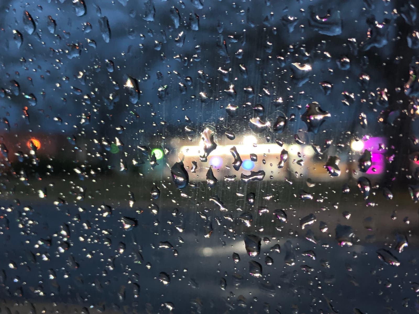 Blurred lights of a small-town street at night seen through a rain-spotted window