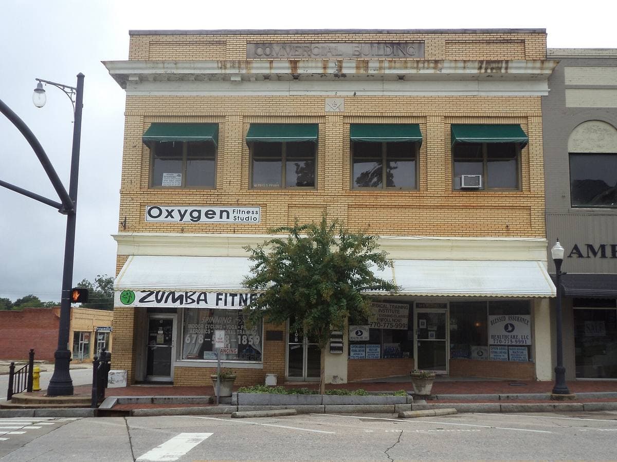A three-storey brick shop building with green awnings on a small-town square