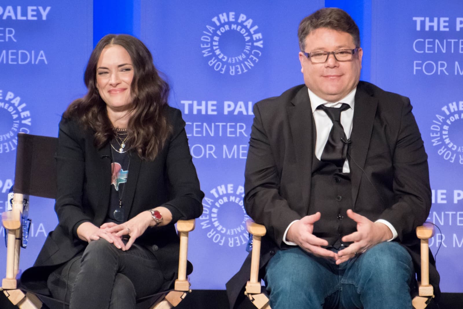 Winona Ryder and Sean Astin sitting side by side on a stage, smiling