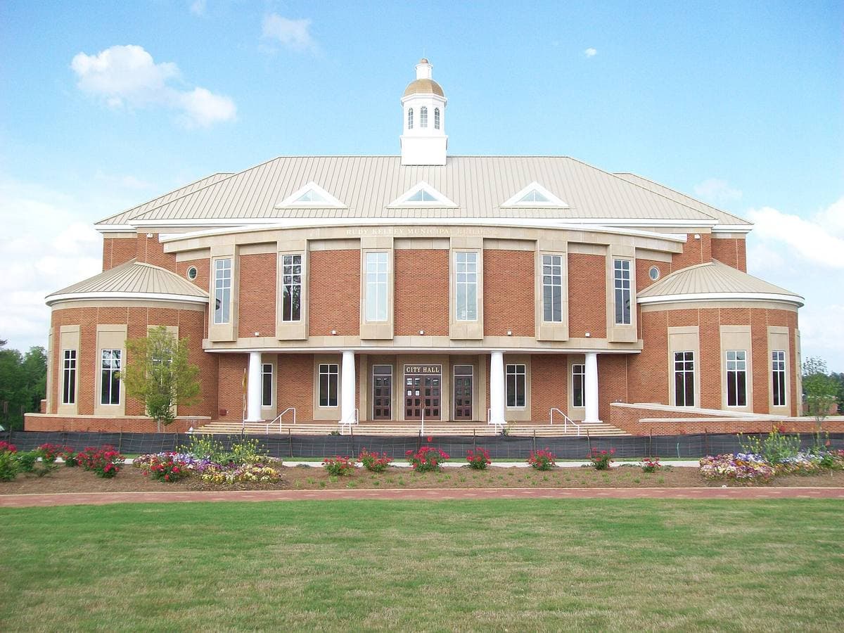A red-brick civic building with a white cupola behind a lawn