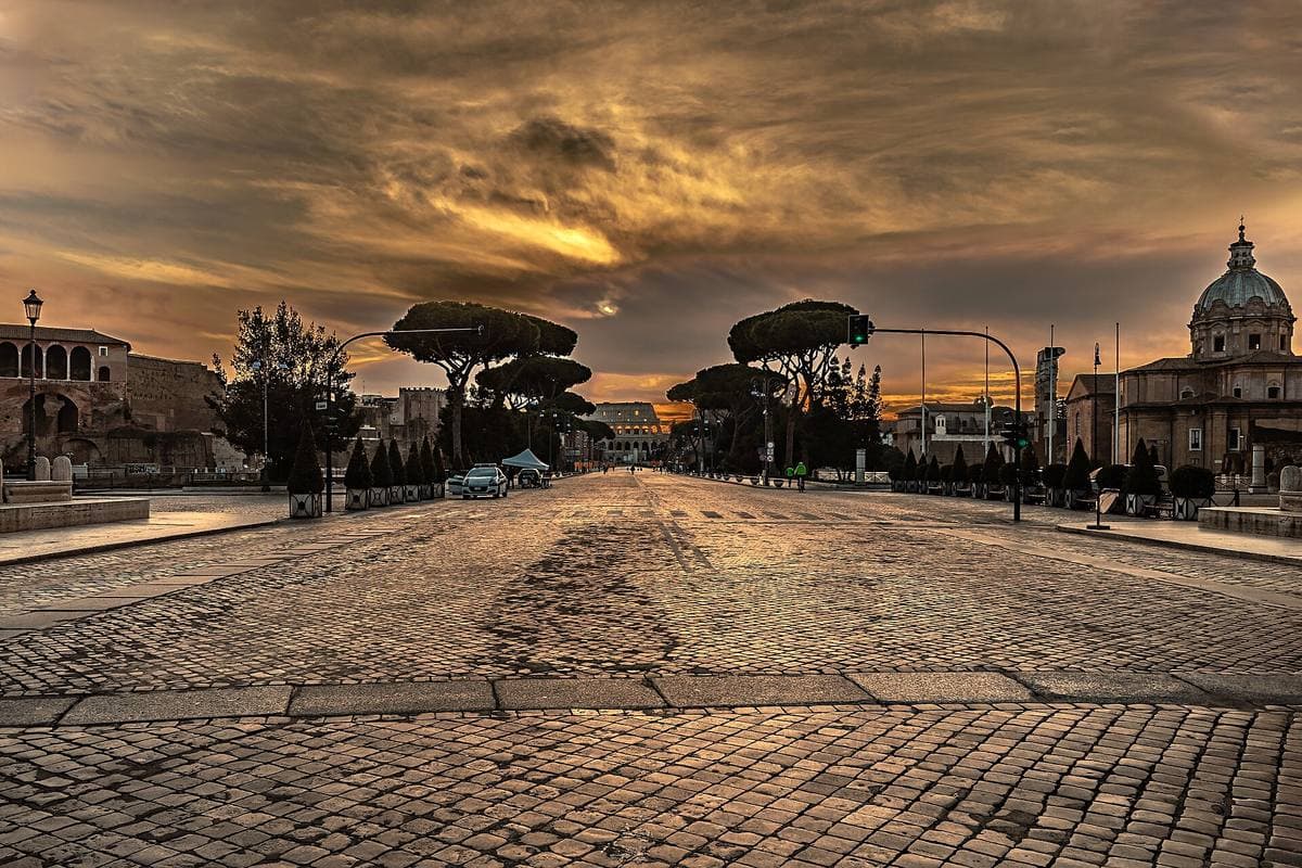 A wide avenue running towards the Colosseum past ancient ruins