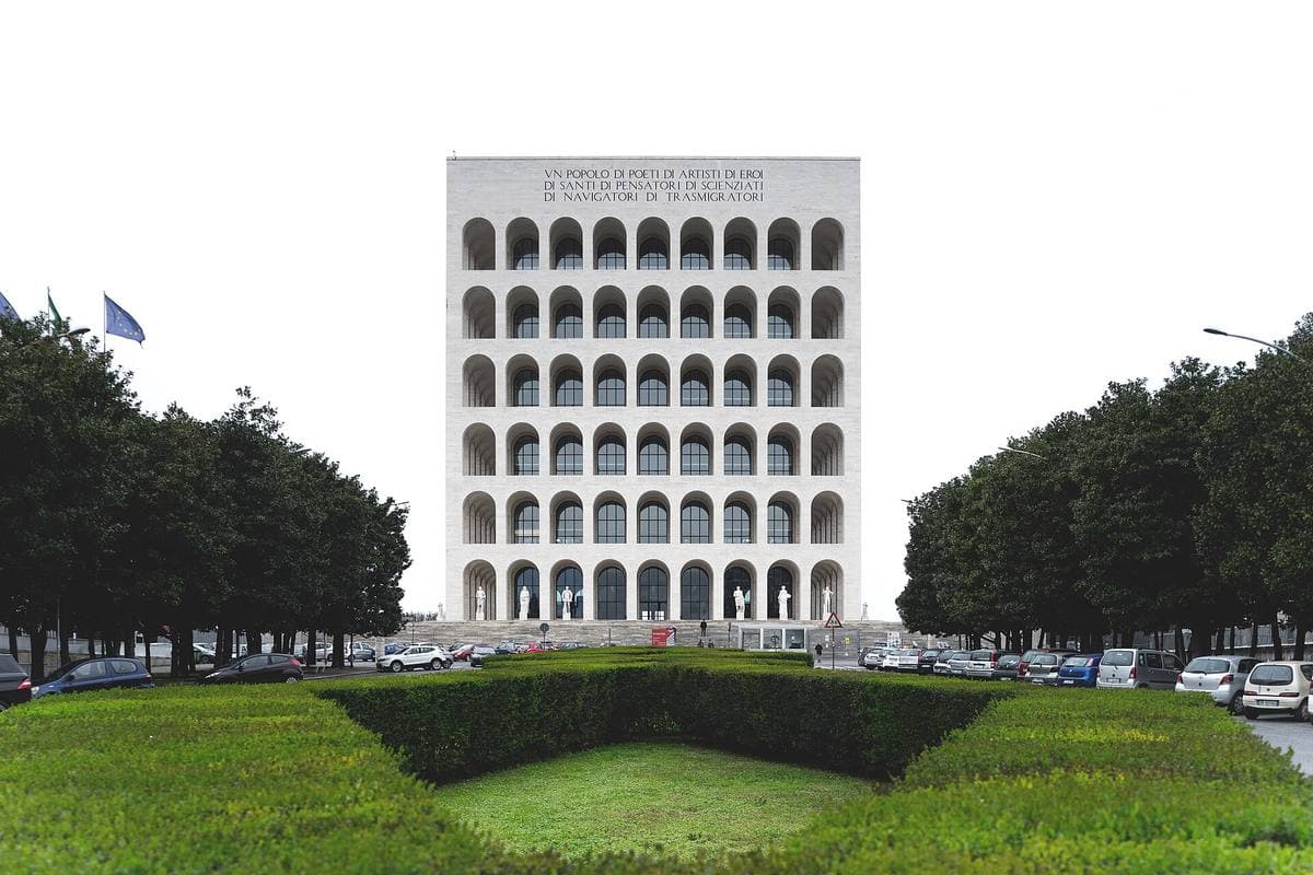 A white cube of stacked arches on a plinth with statues