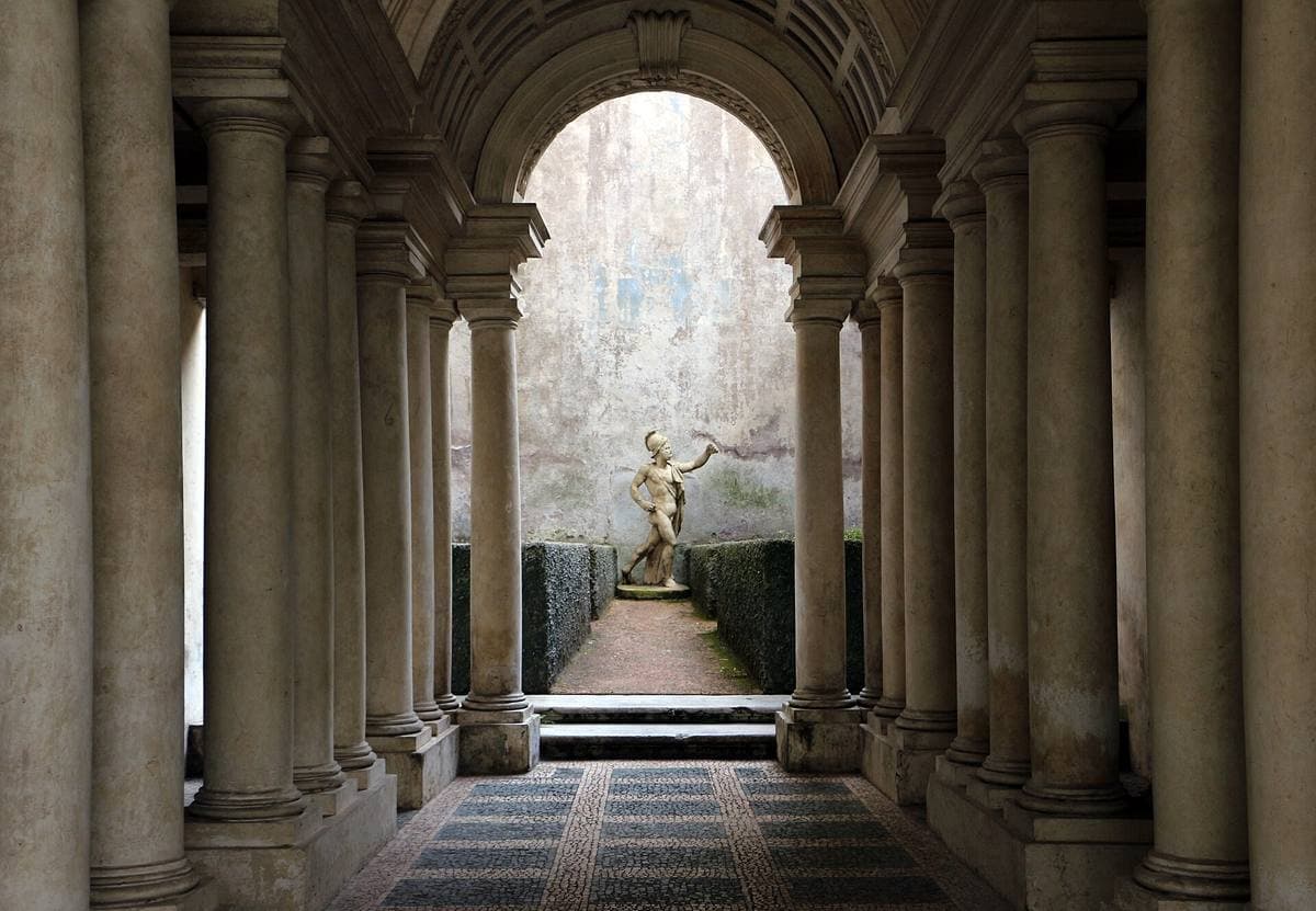 A colonnaded gallery narrowing to a statue framed by hedges