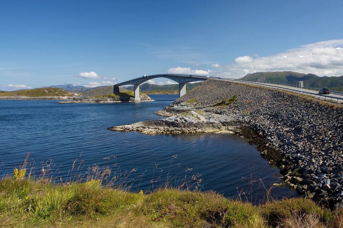 A curving concrete bridge leaping off a rock causeway over blue sea