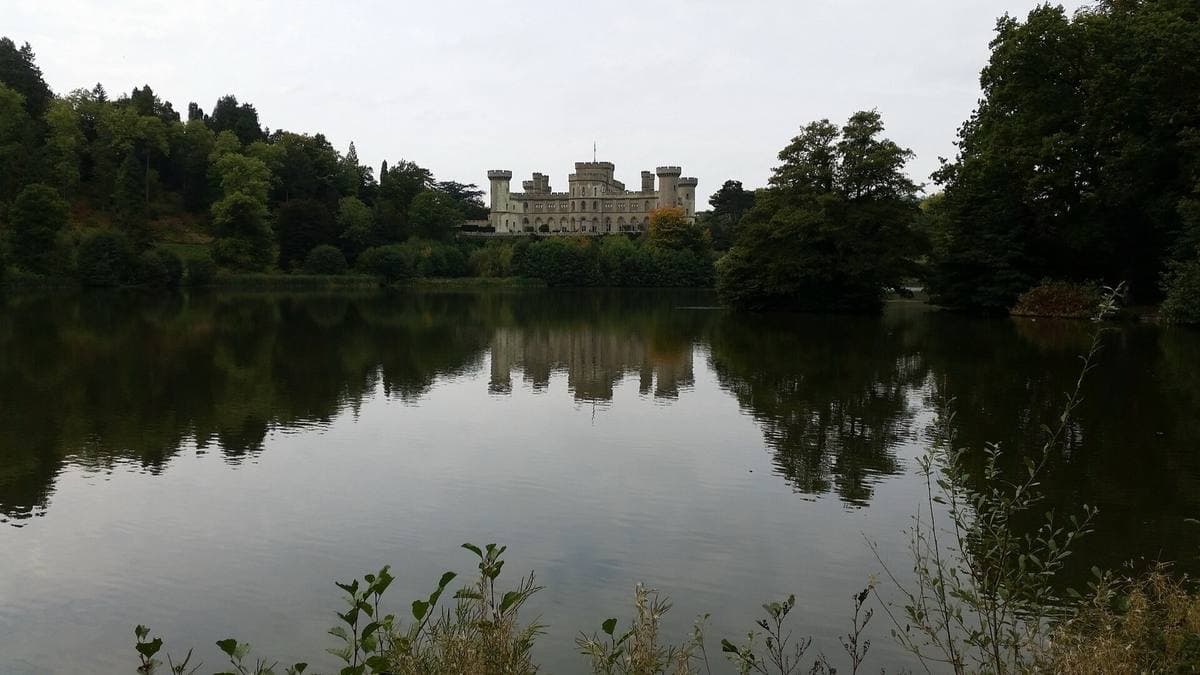 Eastnor Castle’s grey towers low on the horizon, reflected in a still lake between dark trees
