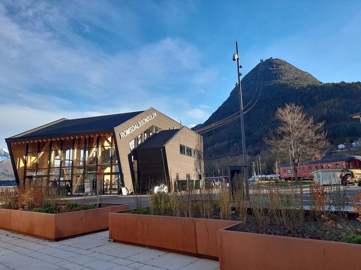 A timber-clad gondola station beside a steep green peak under blue sky