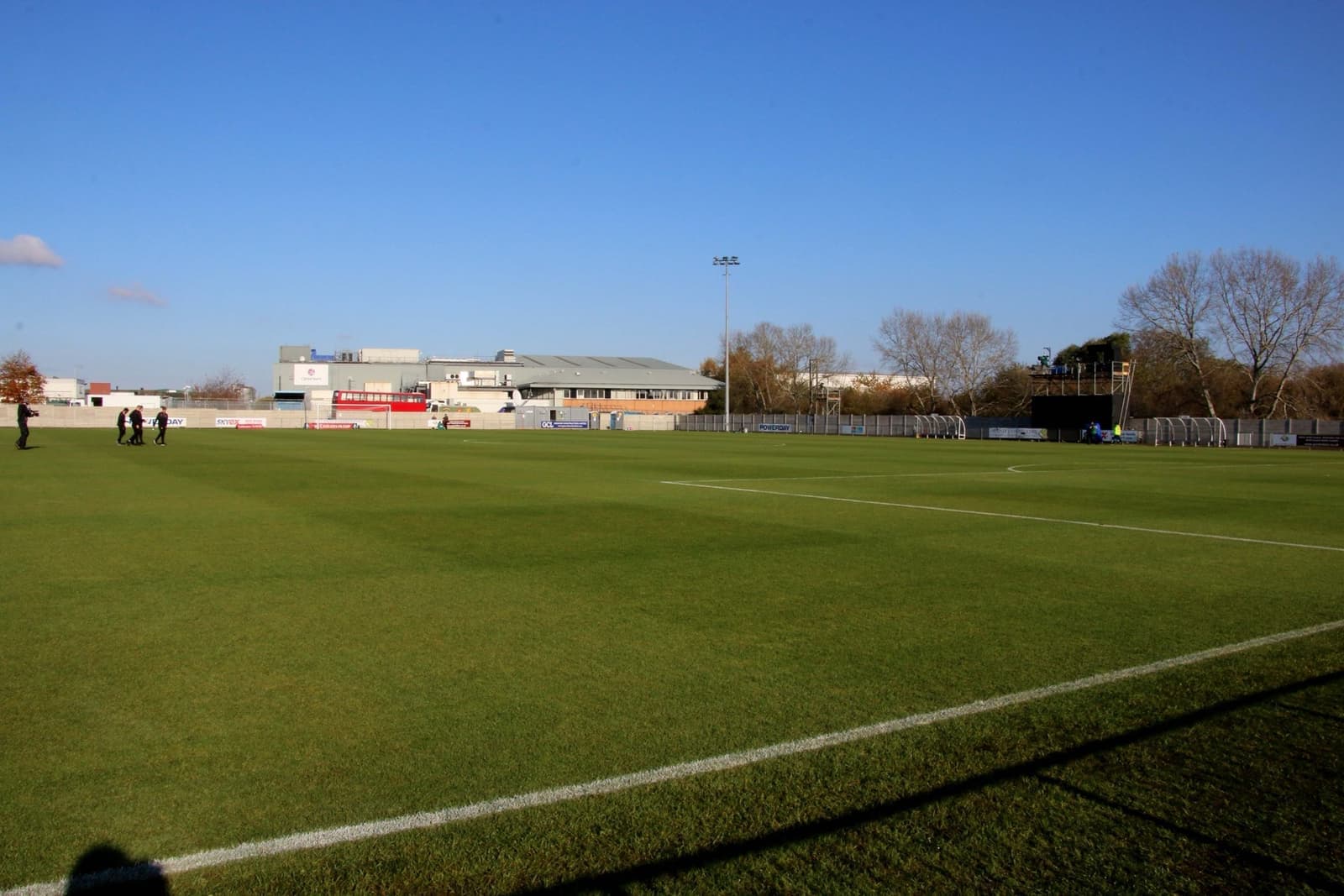 A football pitch in low sun with a small stand and floodlights beyond