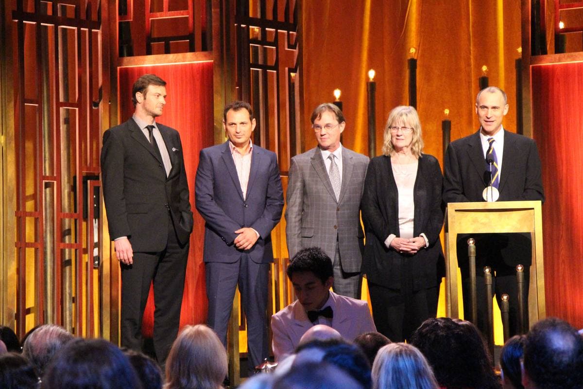 Five people in dark suits on a stage with a lectern