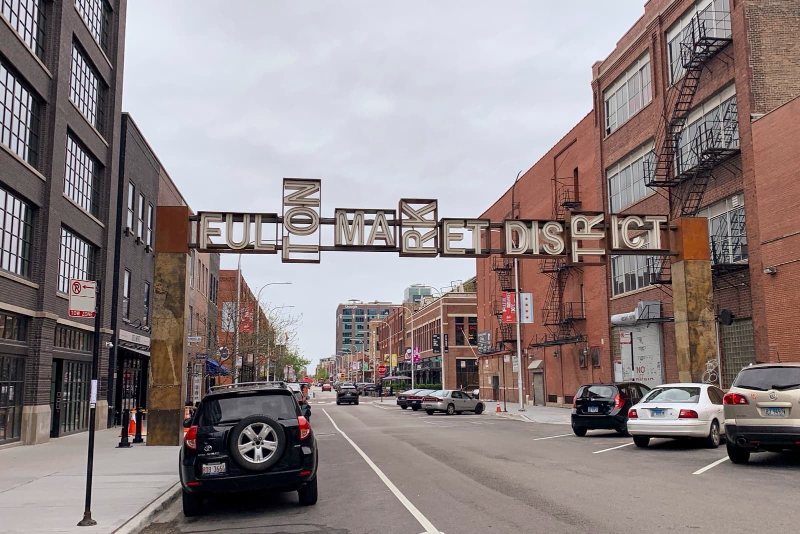 A street of brick warehouses with the Fulton Market District sign arching overhead