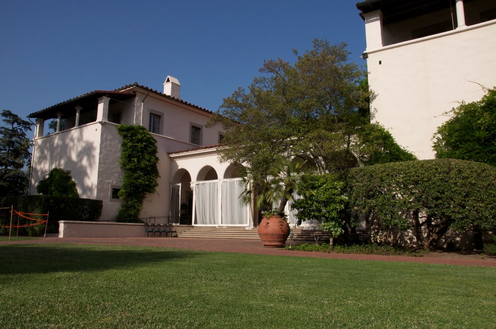 A white Mediterranean-style club house with arches behind a lawn under a deep blue sky