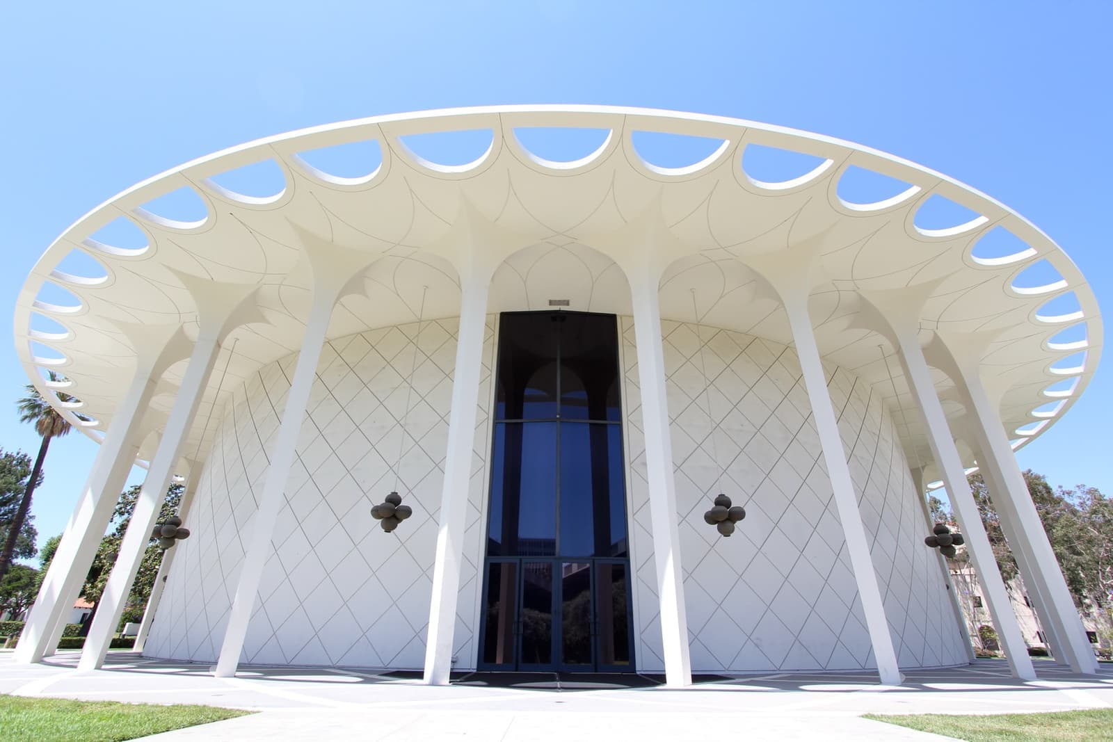 A round white auditorium with a ring of slender columns and a lawn in front