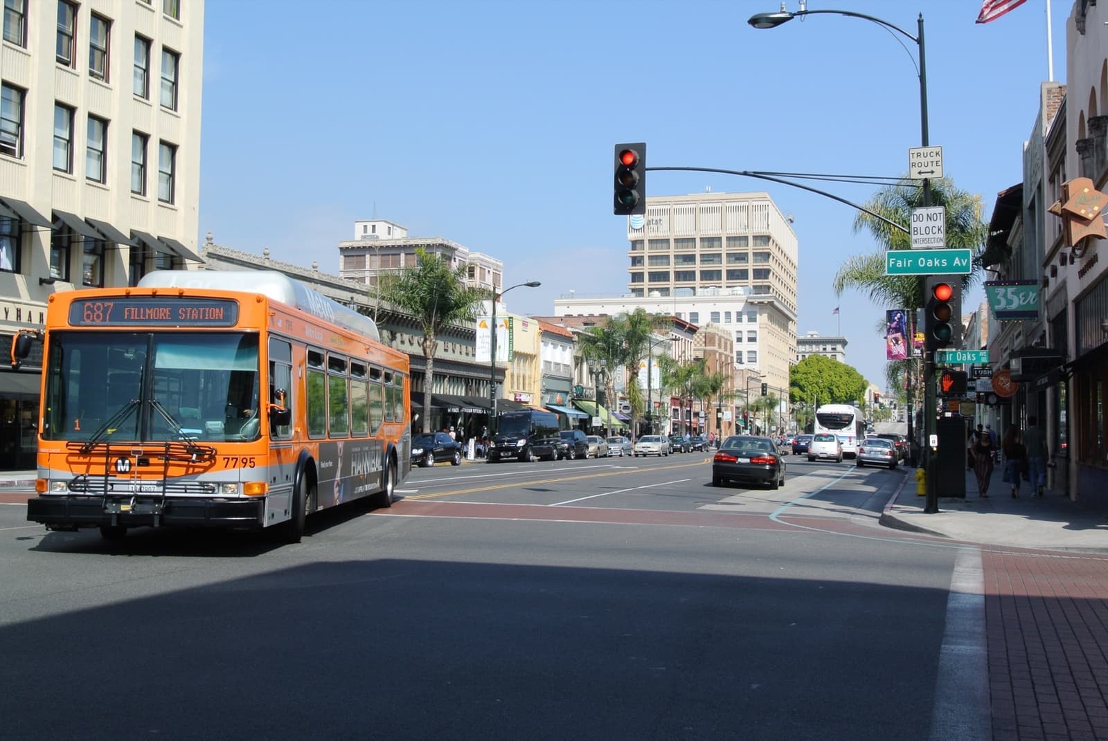 An orange city bus crossing a sunny Old Pasadena junction lined with palms