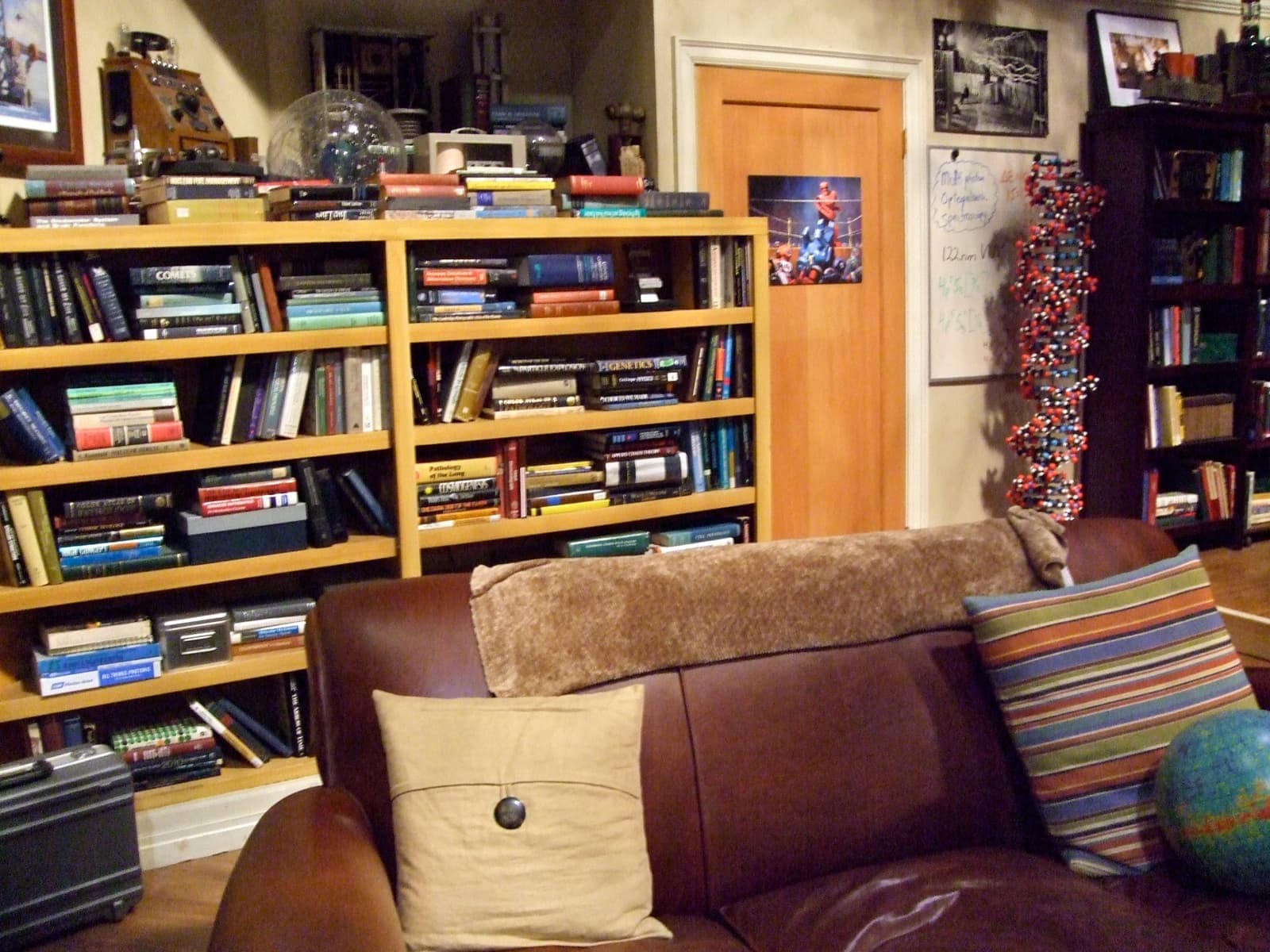 A brown leather couch with striped cushions in front of full bookshelves and an orange door