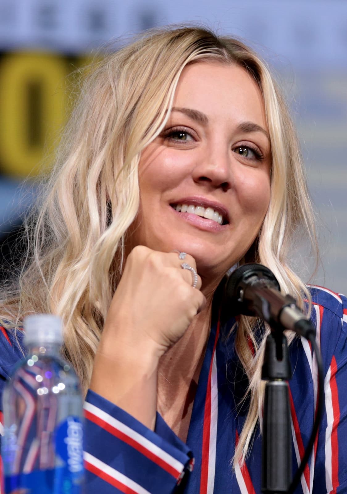 Kaley Cuoco smiling with her chin on her hand behind a microphone